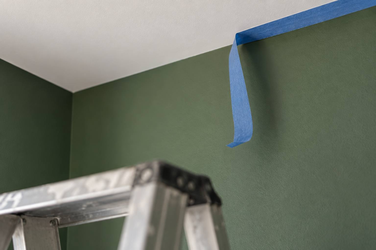 Angle d’un mur vert sauge mat et d’un plafond blanc, ruban de masquage retiré